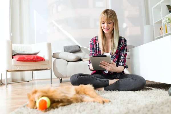 Schöne junge Frau mit ihrem Hund mit digitalem Tablet zu Hause. — Stockfoto