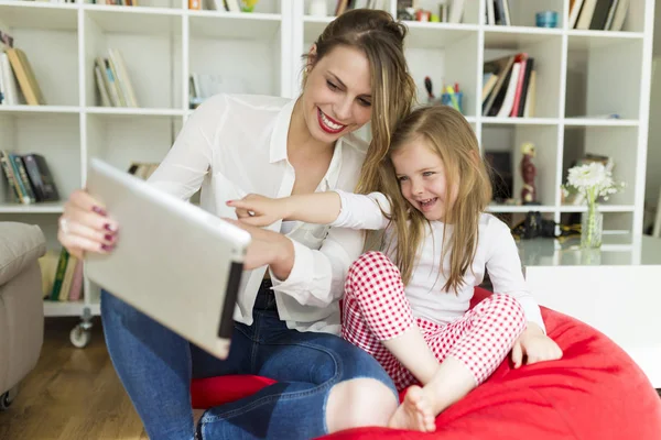 Bela mãe e filha brincando com tablet digital em casa . — Fotografia de Stock