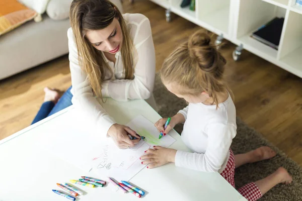 Mooie moeder met haar dochter tekenen met kleurpotloden thuis. — Stockfoto