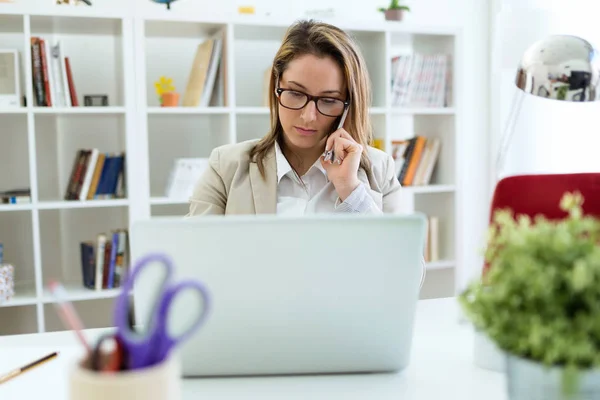 Piękna młoda kobieta, praca z telefonu komórkowego w jej biurze. — Zdjęcie stockowe