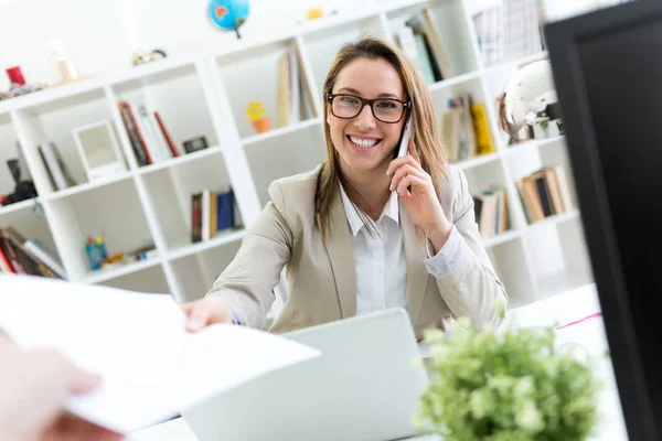 Frumoasa femeie tânără care lucrează cu telefonul mobil în biroul ei . — Fotografie, imagine de stoc