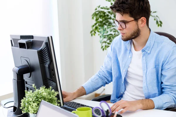 Schöner junger Mann arbeitet mit Laptop im modernen Büro. — Stockfoto
