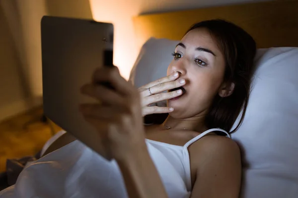 Überraschte Frau schaut ihr digitales Tablet nachts ins Bett. — Stockfoto