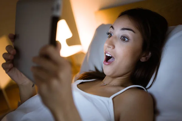 Überraschte Frau schaut ihr digitales Tablet nachts ins Bett. — Stockfoto