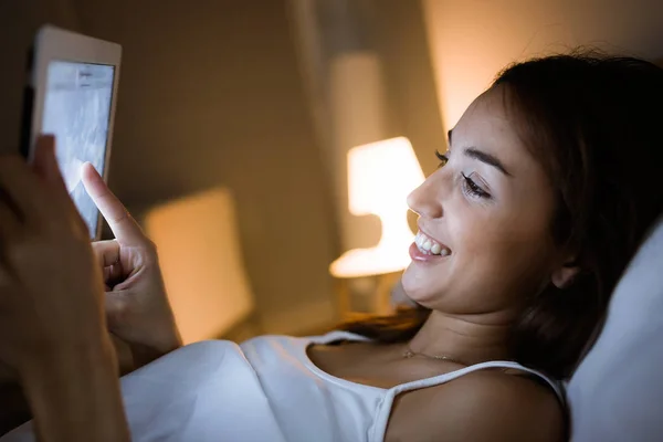 Mulher bonita usando seu tablet digital na cama no nig — Fotografia de Stock