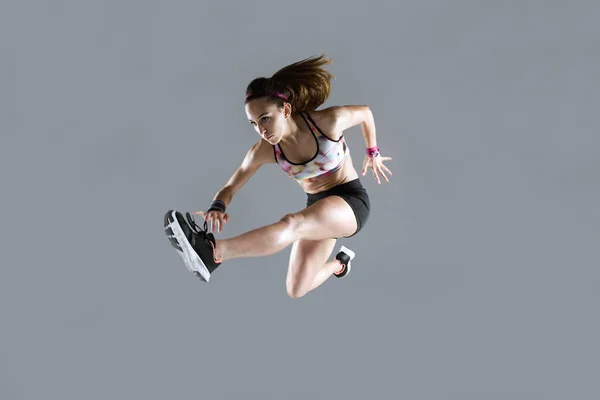 Apto e esportivo jovem mulher pulando no fundo branco . — Fotografia de Stock