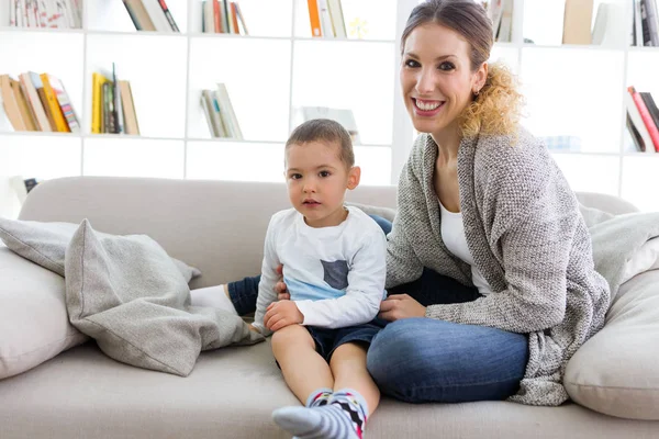 Bela jovem mãe e seu filho olhando para a câmera em casa . — Fotografia de Stock