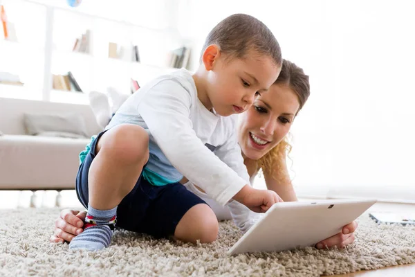 Bella giovane madre e suo figlio utilizzando tablet digitale a casa . — Foto Stock