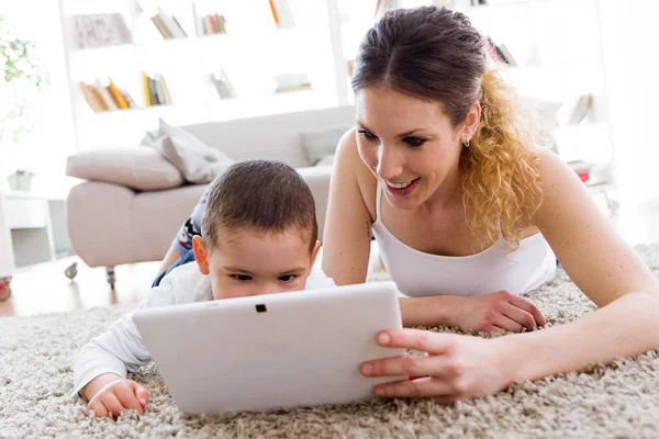 Schöne junge Mutter und ihr Sohn mit digitalem Tablet zu Hause. — Stockfoto