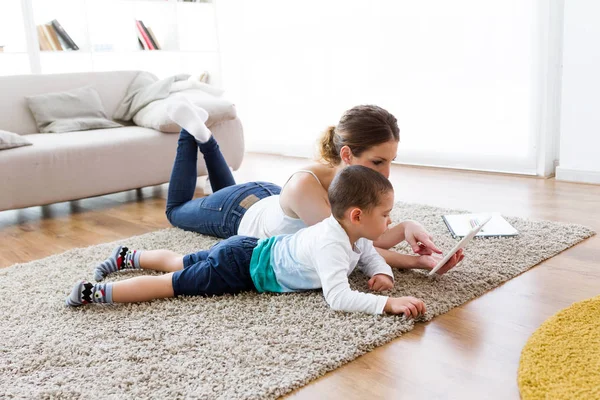 Schöne junge Mutter und ihr Sohn mit digitalem Tablet zu Hause. — Stockfoto