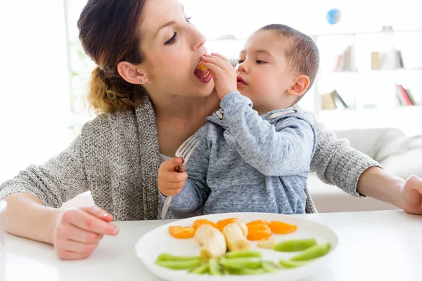 Schöne junge Mutter und ihr Sohn essen Früchte zu Hause. — Stockfoto