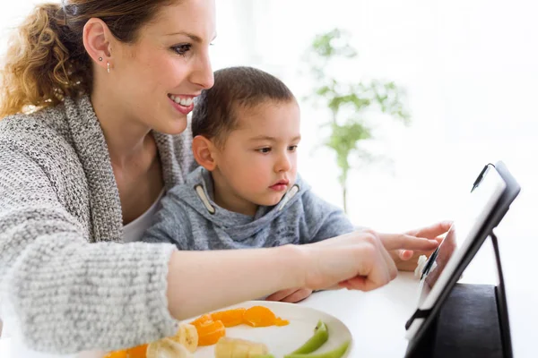 Jeune mère et son fils en utilisant une tablette numérique tout en mangeant des fruits — Photo