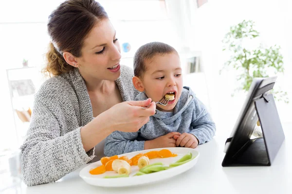 Joven madre y su hijo usando tableta digital mientras come fruta —  Fotos de Stock