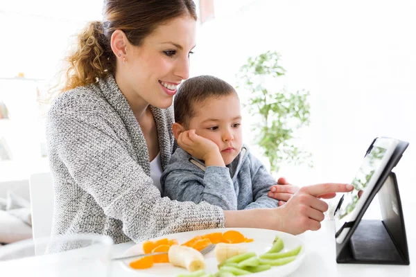 Jonge moeder en haar zoon met behulp van digitale tablet tijdens het eten van fruit — Stockfoto