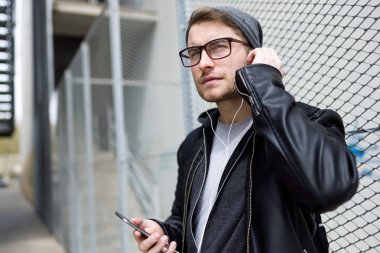 Modern genç adam sokakta cep telefonunuzla müzik dinlemek.