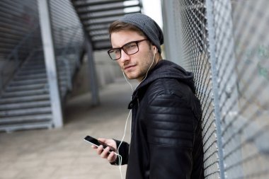 Modern genç adam sokakta cep telefonunuzla müzik dinlemek.