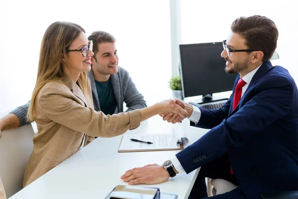 Junges Paar im Bankbüro schüttelt Finanzberater die Hand. — Stockfoto