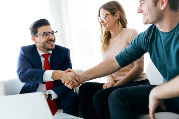 Young couple in bank office shaking hand to financial adviser.