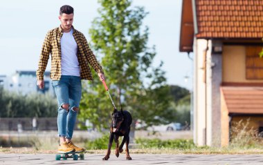 Yakışıklı genç adam köpeğiyle parkta kaykay.
