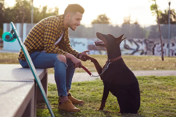 ชายหนุ่มหล่อเล่นกับสุนัขของเขาในสวนสาธารณะ . — ภาพถ่ายสต็อก