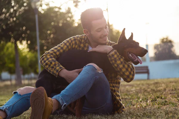 Un tânăr chipeș se joacă cu câinele său în parc . — Fotografie, imagine de stoc