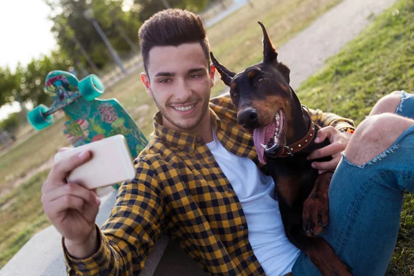 Pemuda tampan dengan anjingnya menggunakan ponsel di taman. . — Stok Foto