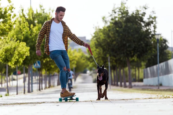 Yakışıklı genç adam köpeğiyle parkta kaykay. — Stok fotoğraf
