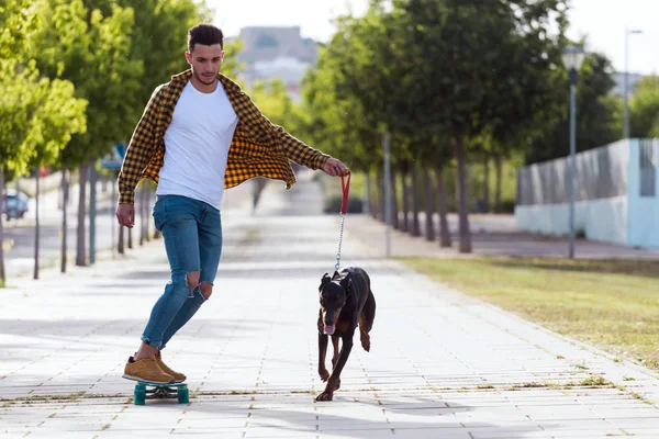 Joven guapo con su perro patinando en el parque . — Foto de Stock