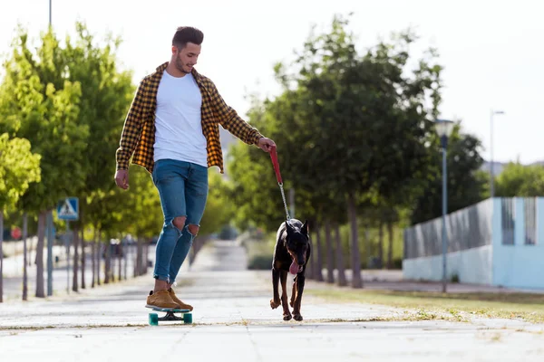 Yakışıklı genç adam köpeğiyle parkta kaykay. — Stok fotoğraf