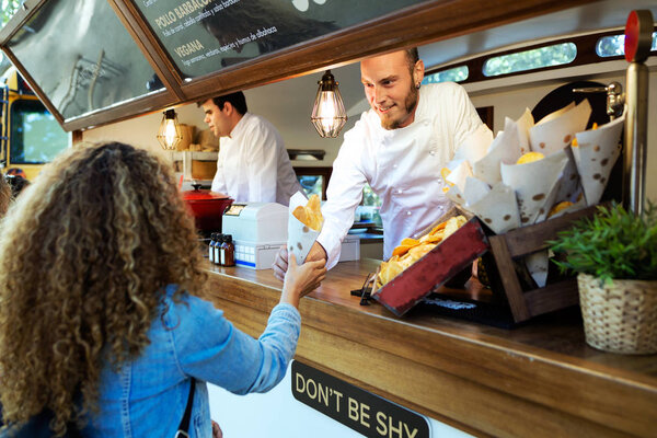 Beautiful young woman buying barbecue potatoes on a food truck.