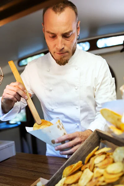 Jovem chef que serve batatas de churrasco em um caminhão de comida . — Fotografia de Stock