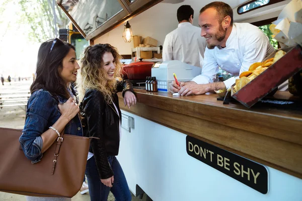 Twee mooie jonge vrouwen eten bestellen van de kok van een food truck. — Stockfoto