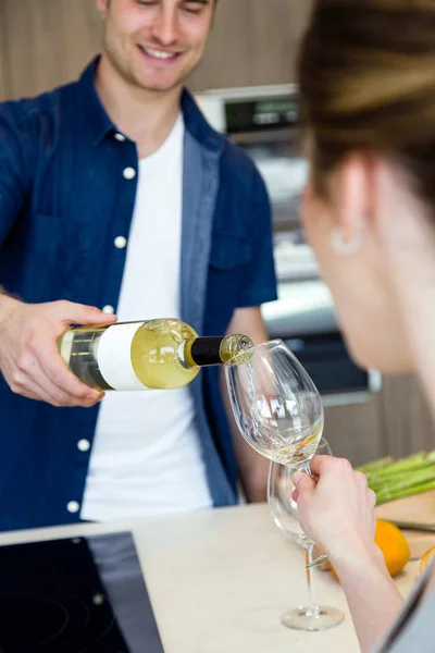Przystojny, młody człowiek, otwierając butelkę wina, podczas gdy jego żona za pomocą cyfrowego tabletu w kuchni. — Zdjęcie stockowe