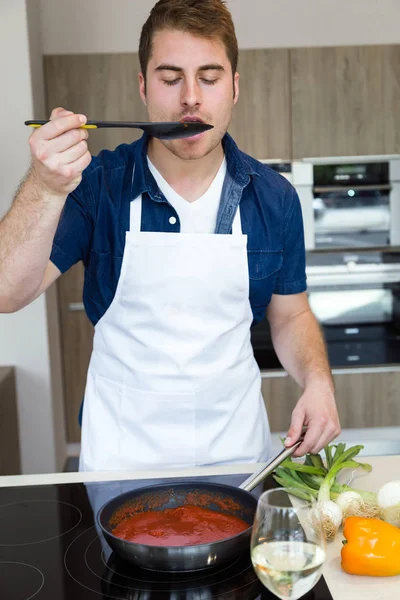 Bonito jovem cozinhar molho de tomate na cozinha em casa . — Fotografia de Stock