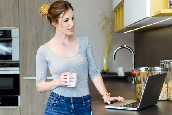 Belle jeune femme utilisant son ordinateur portable dans la cuisine à la maison . — Photo