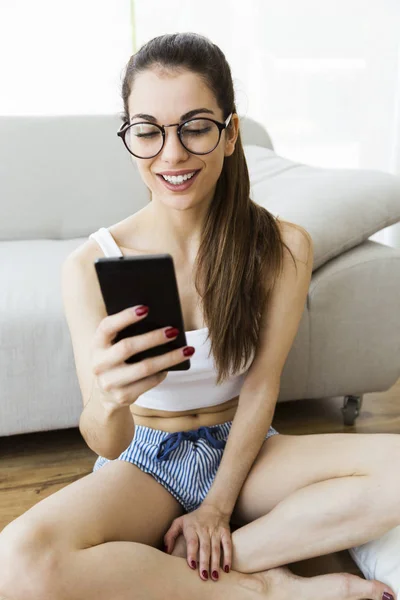 Mooie jonge vrouw met behulp van haar mobiele telefoon thuis. — Stockfoto