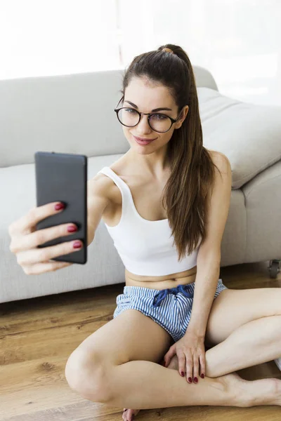 Mooie jonge vrouw met behulp van haar mobiele telefoon thuis. — Stockfoto