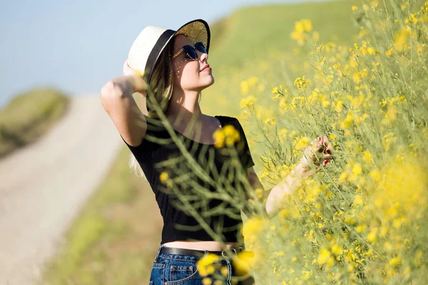 Krásná mladá žena s květinami se těší letní v poli. — Stock fotografie