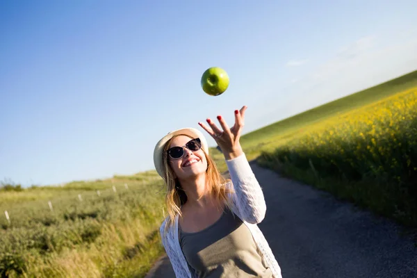 Schöne junge Frau isst einen Apfel auf einem Feld. — Stockfoto