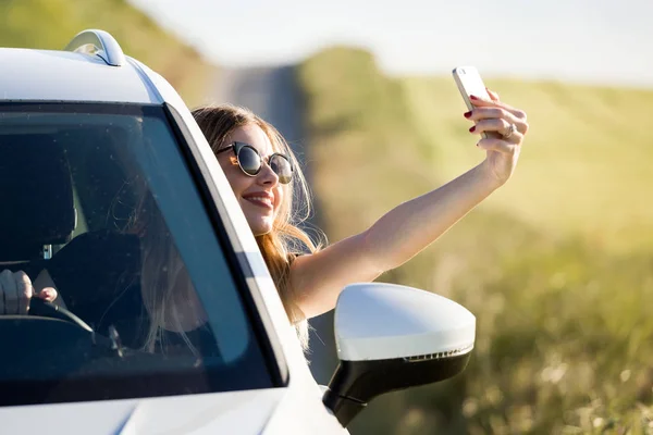 Piękna młoda kobieta, biorąc selfie w samochodzie zaparkowanym w fie — Zdjęcie stockowe