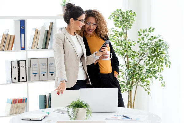 Deux jeunes femmes d'affaires travaillant avec un téléphone portable dans le bureau . — Photo