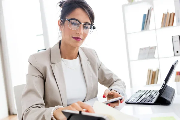 Mooie jonge zakenvrouw met behulp van haar mobiele telefoon in het kantoor. — Stockfoto