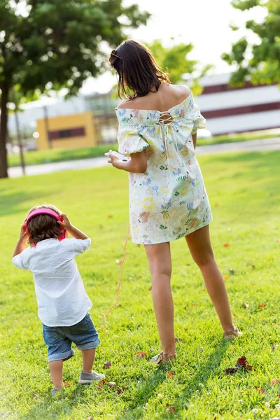 공원에서 음악을 듣고 그녀의 아들과 함께 아름 다운 젊은 어머니. — 스톡 사진