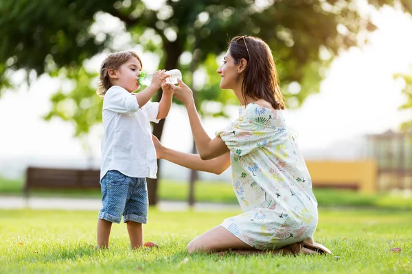 Красива мати дає дитині напій води в парку . — стокове фото