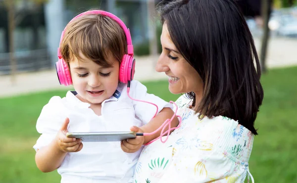 Belle jeune mère avec son fils écoutant de la musique dans le parc . — Photo