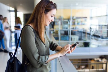 Güzel öğrenci bir üniversitede cep telefonu kullanarak.
