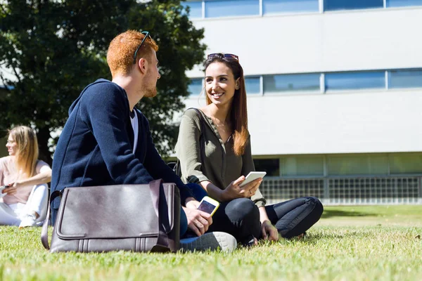 Glada studenter sitta utanför på campus vid universitetet. — Stockfoto