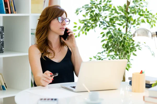 Schöne junge Frau, die zu Hause mit ihrem Handy arbeitet. — Stockfoto