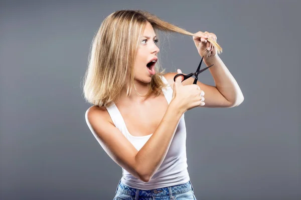 Красивая молодая женщина стрижет волосы на сером фоне . — стоковое фото