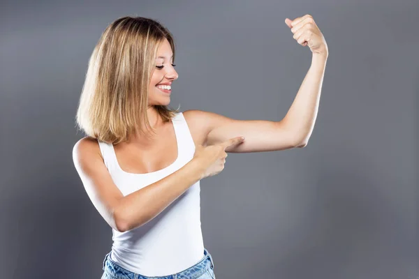 Krásná mladá žena ukazující biceps nad šedým pozadím. — Stock fotografie